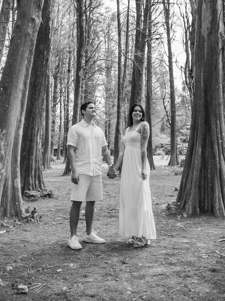 Renan e a esposa de mãos dadas numa floresta, em preto e branco